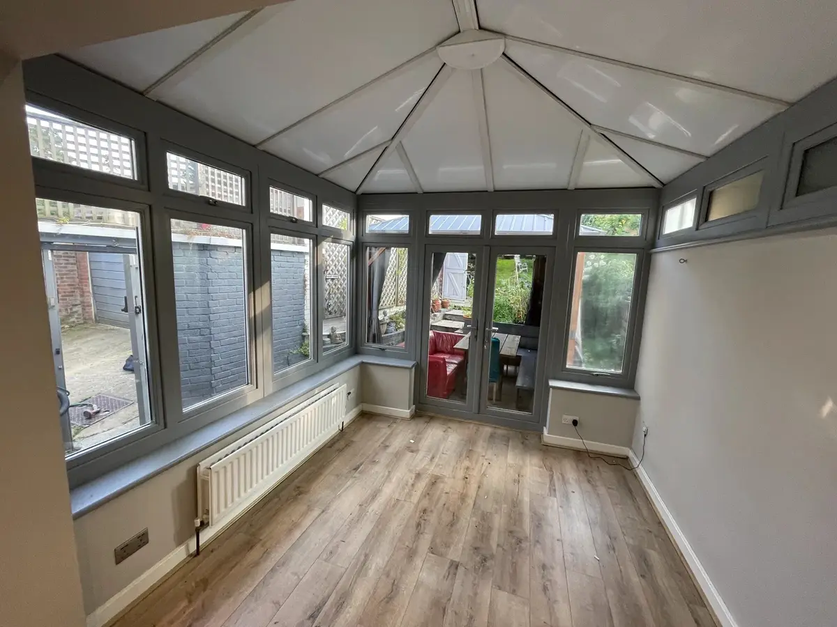 Bright white insulated ceiling panels over oak-effect floorboards in a conservatory with grey frames