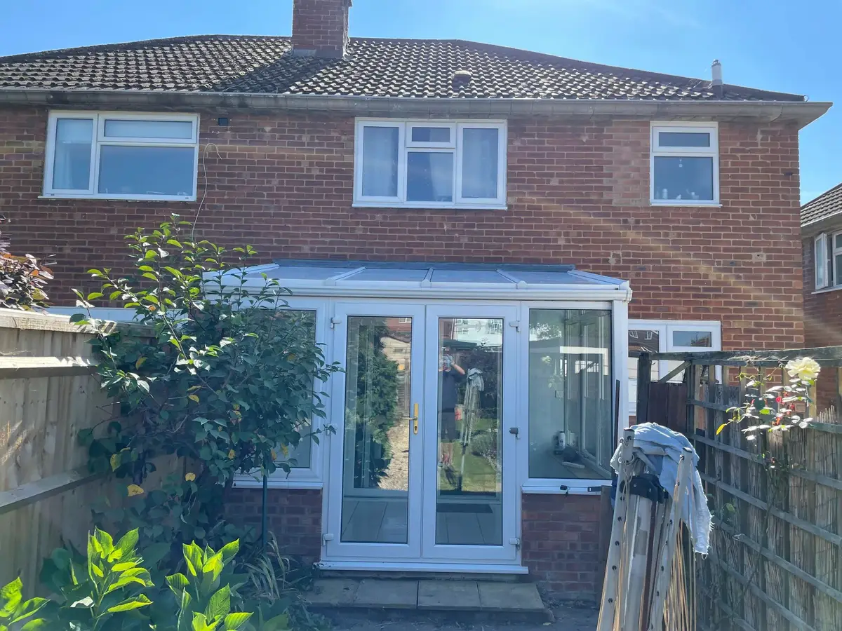 Lean-to conservatory with a completed white panel roof behind a red brick semi