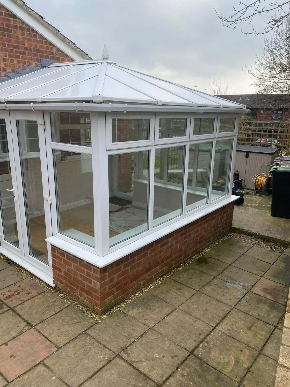 White conservatory on a paved patio, viewed from the corner with its new panel roof