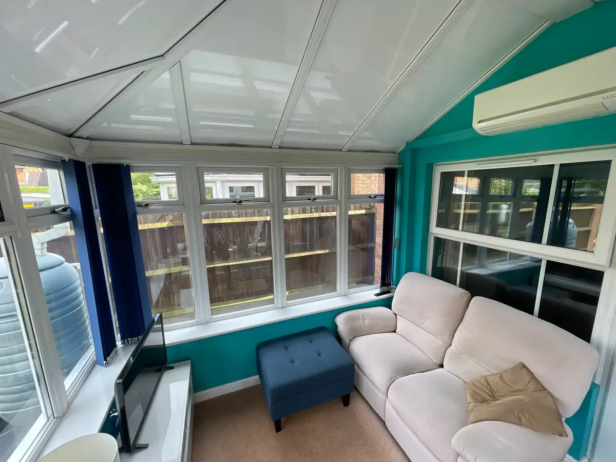 Cream sofa and air conditioner in a conservatory sitting room beneath a white panel roof