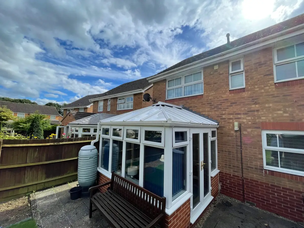 Broad shot of a brick house rear with a Victorian conservatory now wearing a completed white panel roof