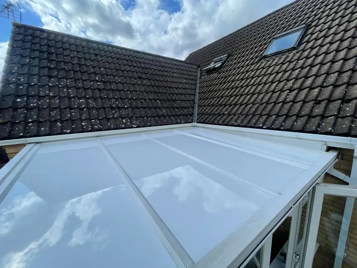 Clouds mirrored in new white roof panels on a conservatory, with a dark bungalow roof behind