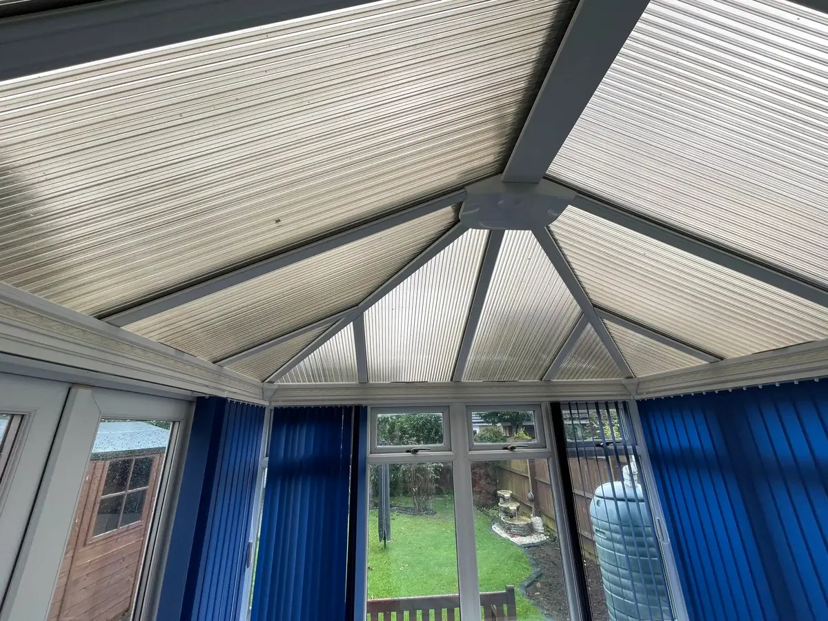 Upward view of an old polycarbonate conservatory roof, facing the doors to the garden
