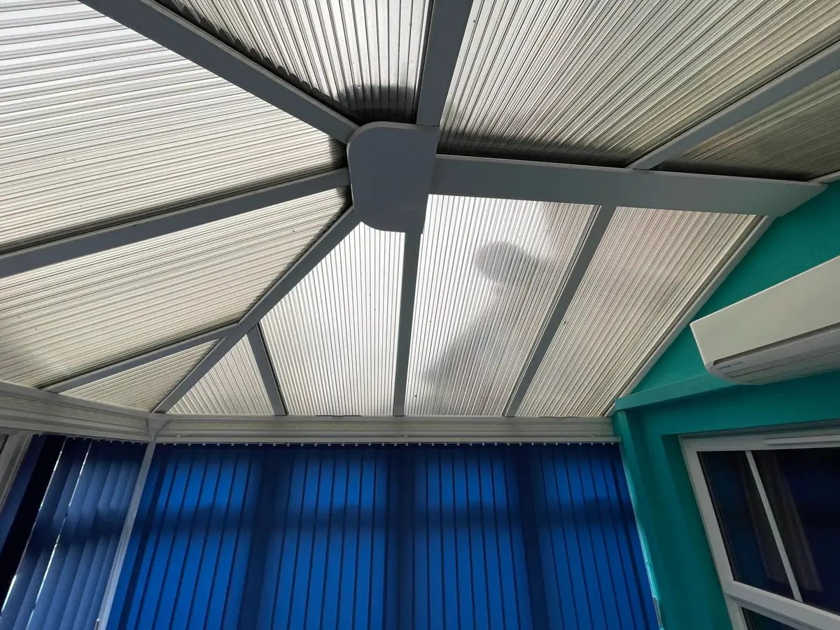 Teal walls, blue blinds and a ribbed polycarbonate roof overhead in a conservatory