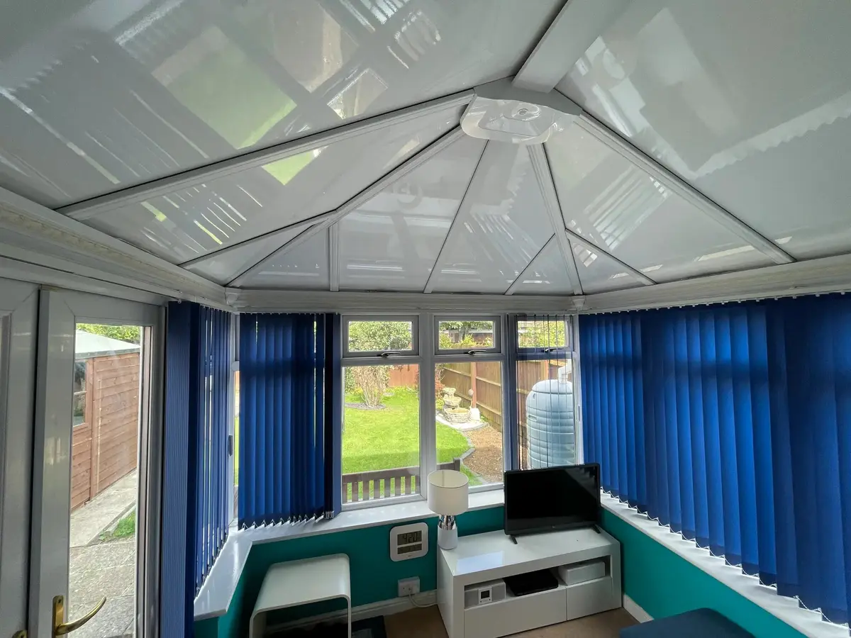 New white insulated ceiling above blue blinds and teal-painted walls in a conservatory