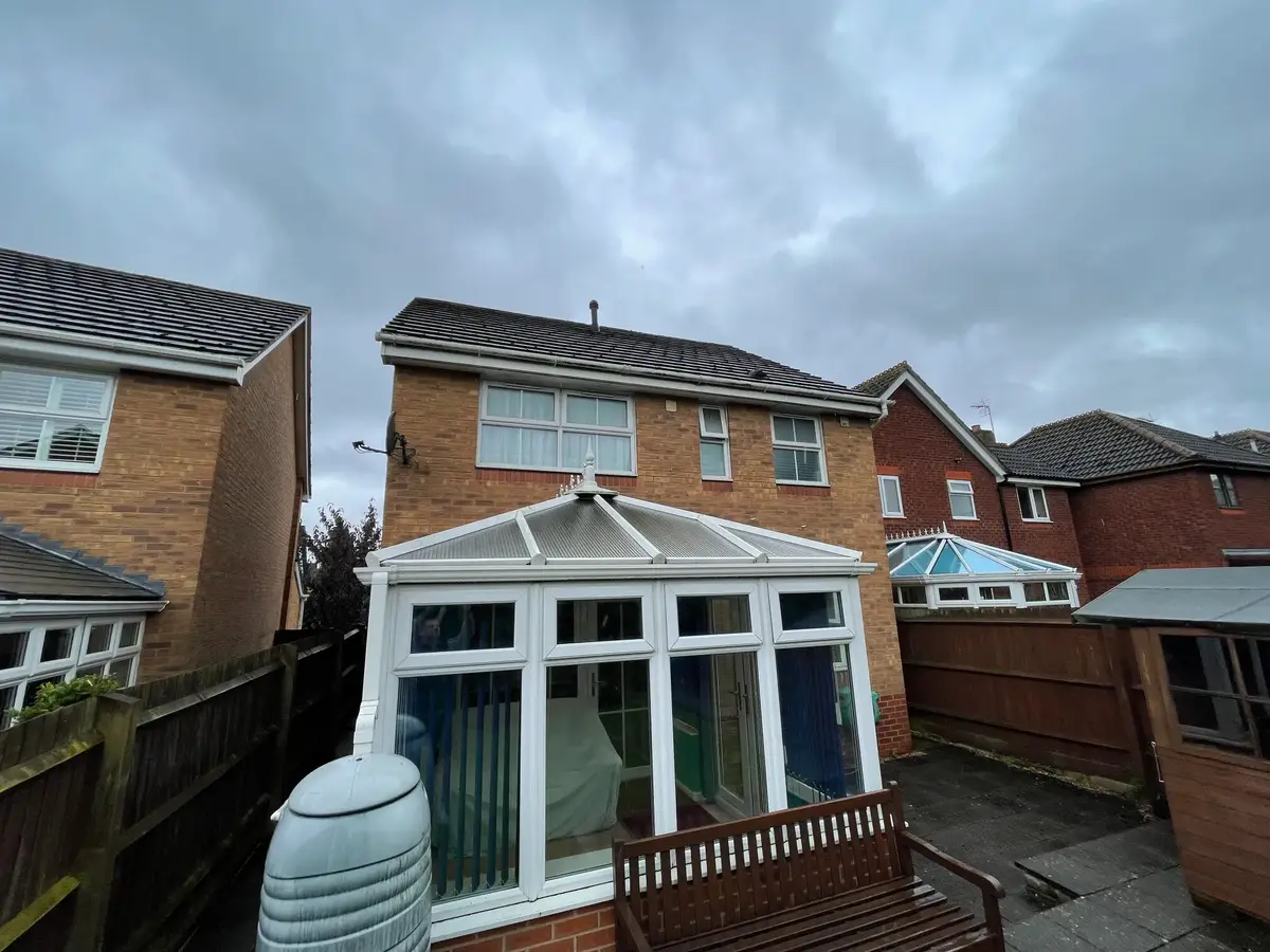 Overcast day at a brick semi, with a white Victorian conservatory under polycarbonate roofing