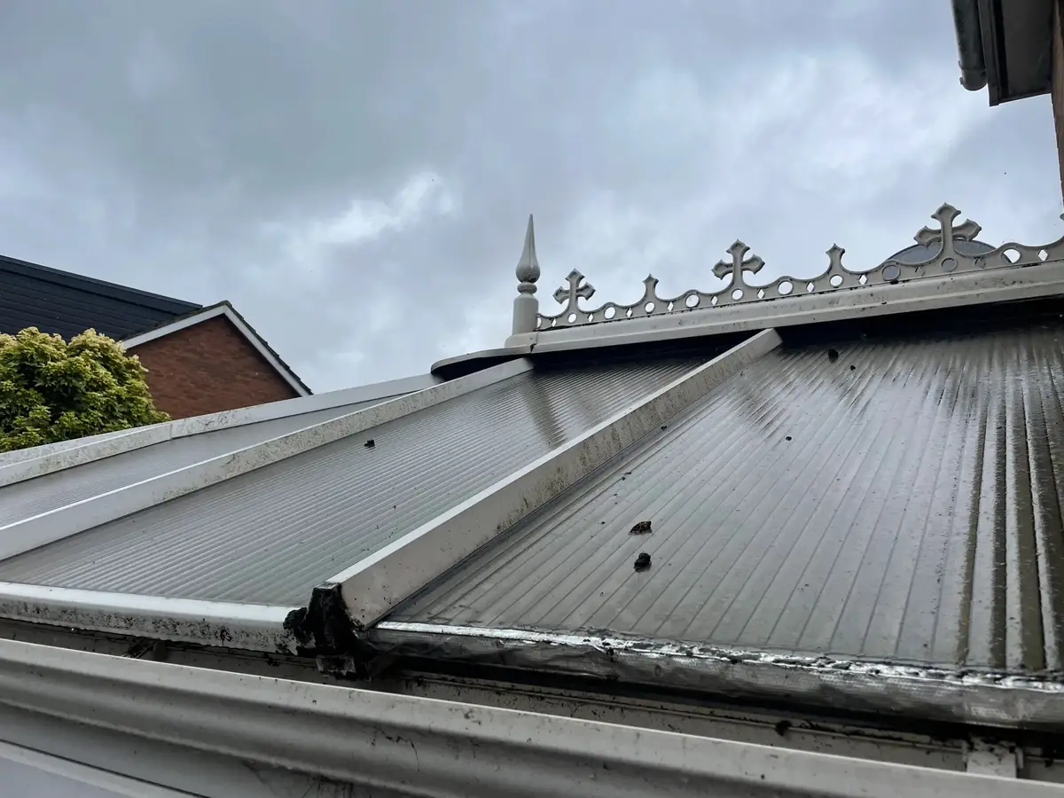 Close view of ridge cresting, glazing bars and worn polycarbonate sheets atop a Victorian conservatory