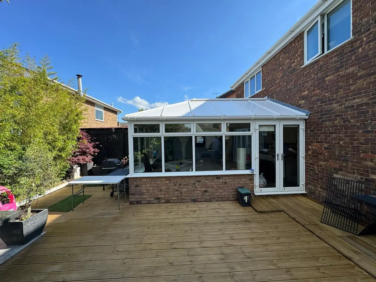 Timber decking laid before a white conservatory now wearing its completed insulated roof